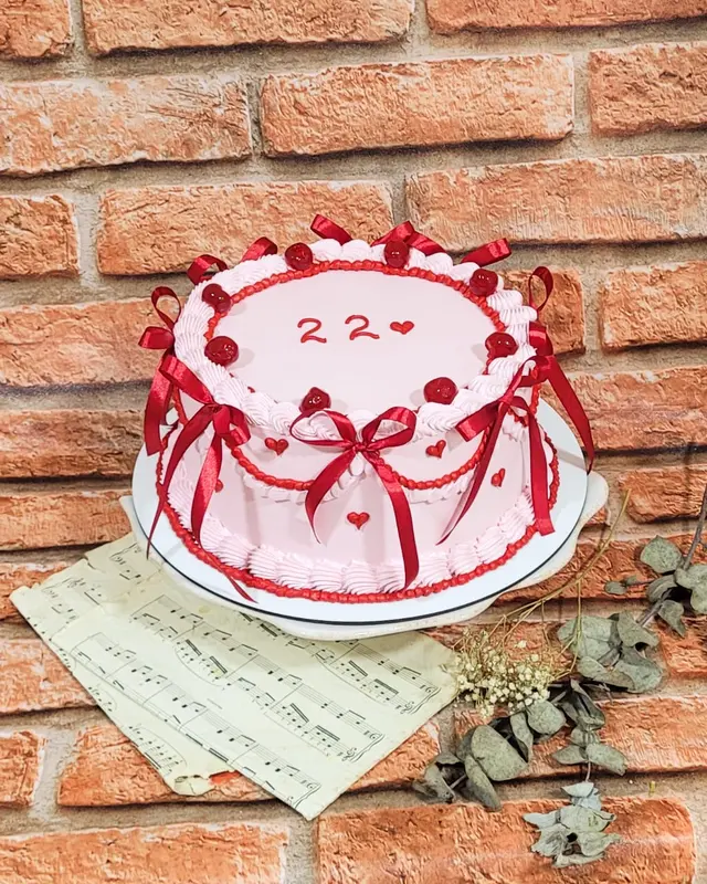Bolo branco com laço vermelho, bolinhas e o número 22 no topo