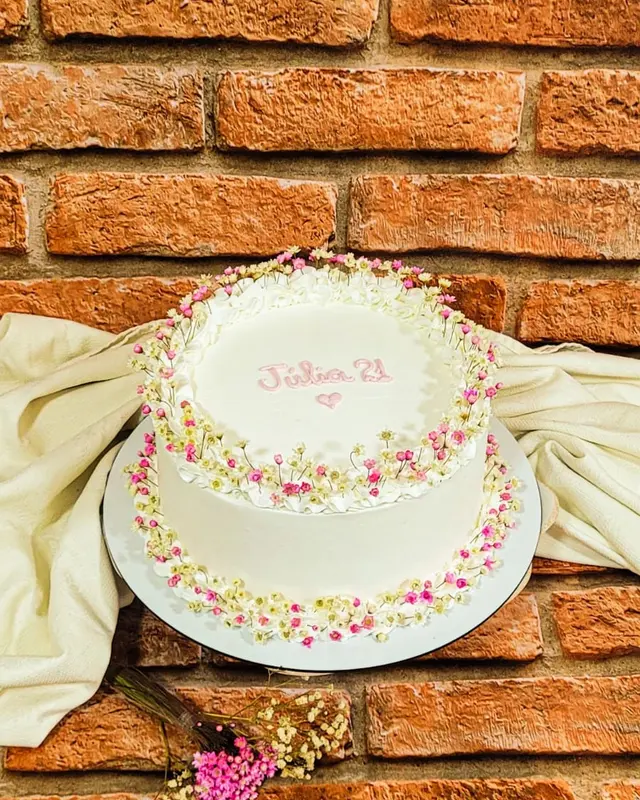 Bolo branco com confeites coloridos e nome escrito à mão no topo