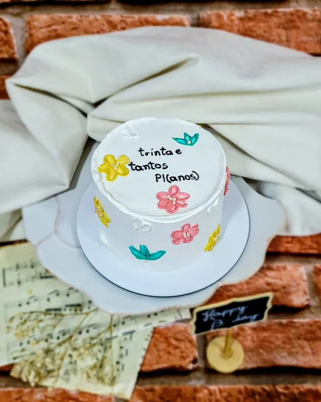 Bolo branco com flores pintadas à mão e a frase trinta e tantos pl(anos)