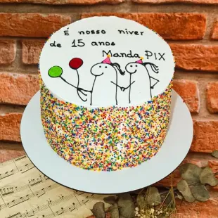 Bolo coberto de confeites coloridos, com desenho e frase escritos à mão no topo