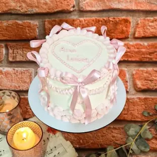 Bolo rosa com laços, pérolas e um coração escrito à mão